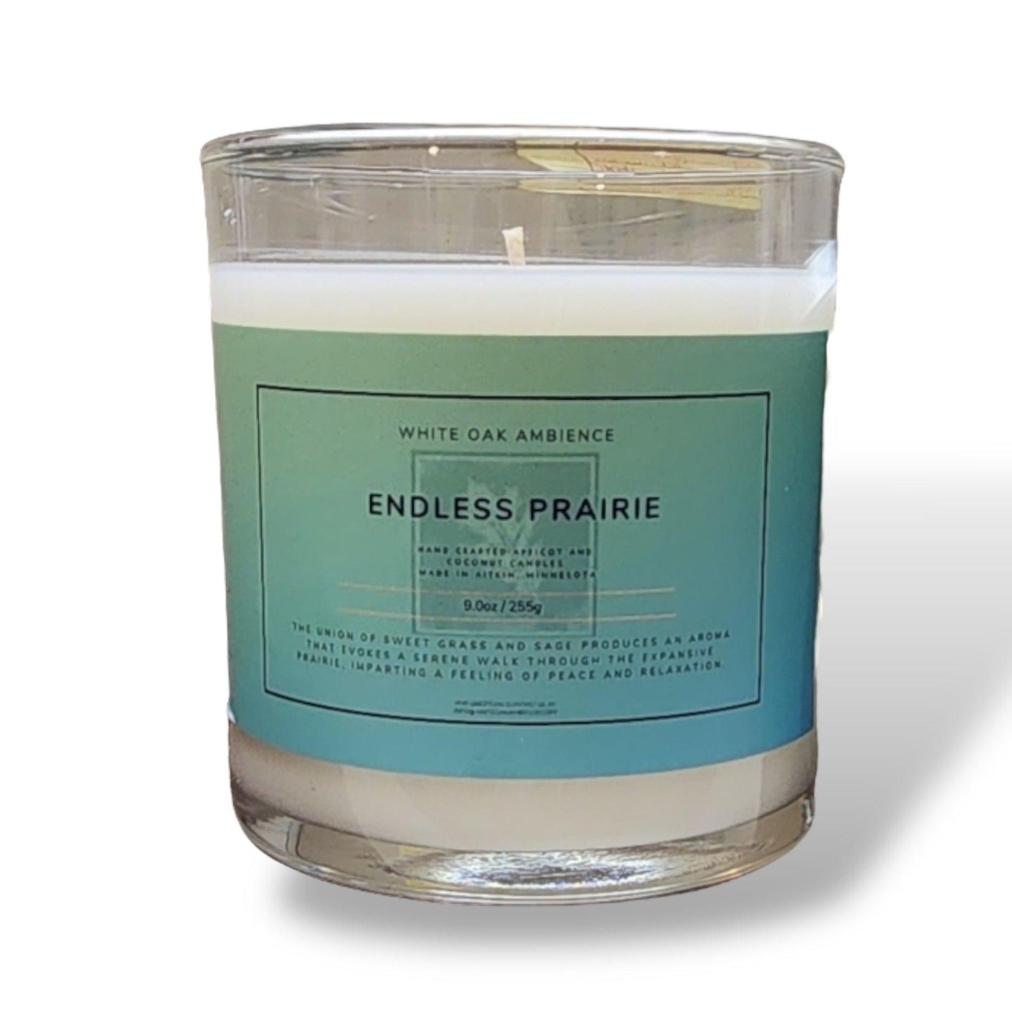 A clear glass candle with a label that reads 'White Oak Ambience Endless Prairie'. The candle appears to be made of an apricot-coconut wax blend and has a white cotton wick.