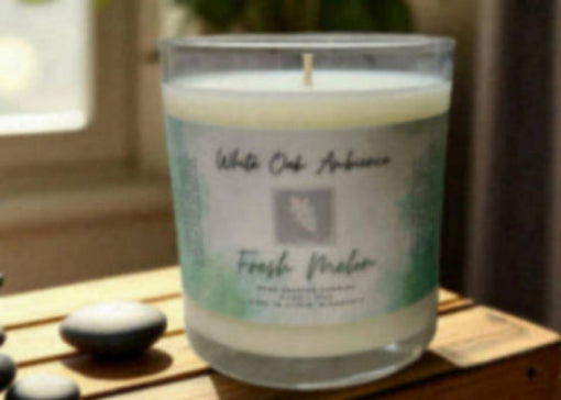Candle labeled 'White Oak Ambience' on a wooden surface with a plant in the background